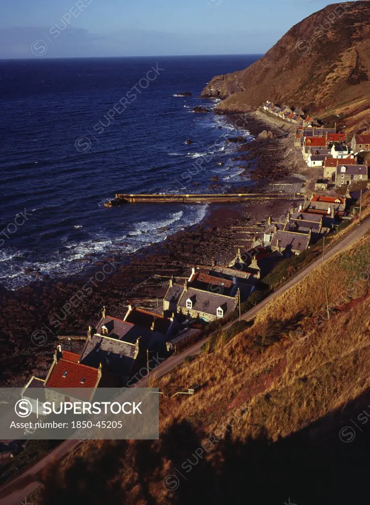 One time fishing village seen from cliff top. Row of cottages at foot of steep hillside overlooking coast and stone jetty.Scotland Aberdeenshire Crovie