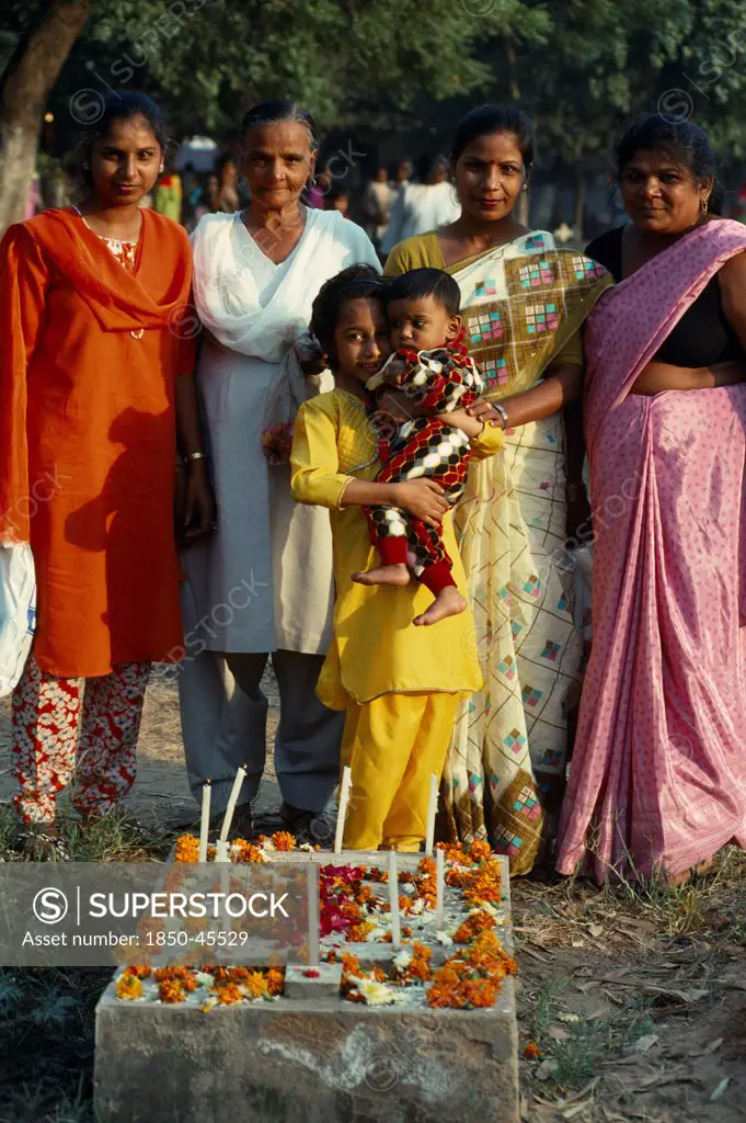 India, Delhi, All Souls Day in Christian cemetary, family group around grave decorated with flowers and candles.