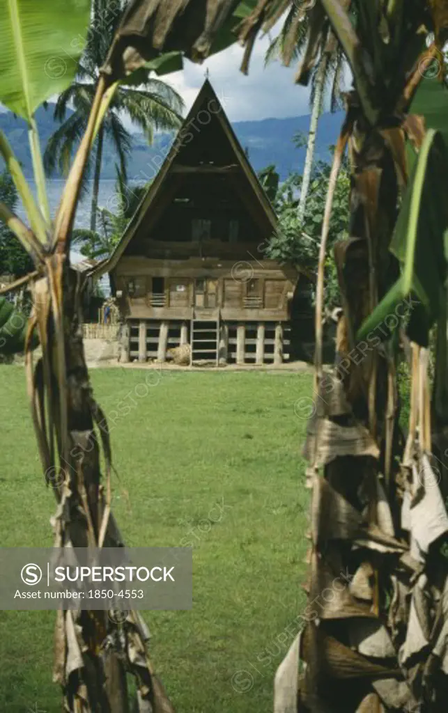 Indonesia, Sumatra, Lake Toba , Wooden Batak House With Pointed Roof On Samosir Island Seen Through Banana Trees
