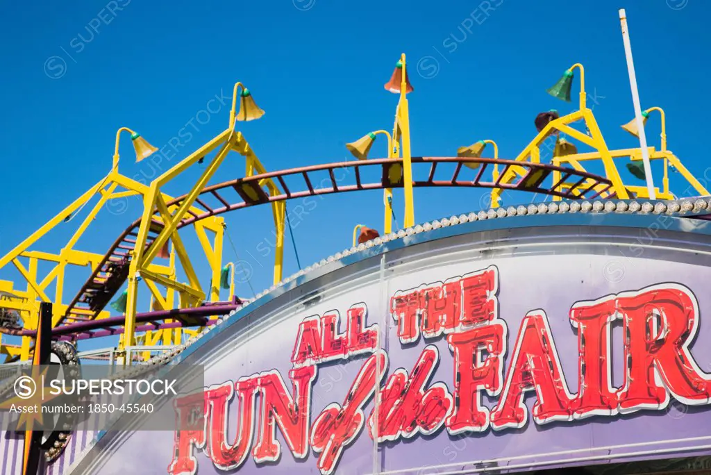 England, Lincolnshire, Skegness, Facade of amusement arcade with rollercoaster behind in clear blue sky.