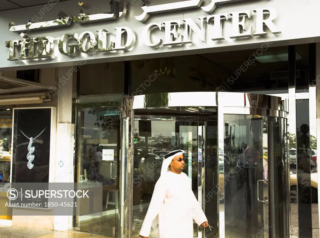 UAE , Dubai, Emirati Arab man in Dishdasha passes Gold Center at Gold Souk Deira.