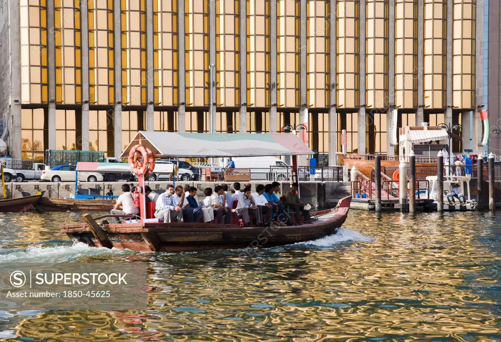 UAE , Dubai, Abra water taxi taking commuters across the Creek with bank facade behind.