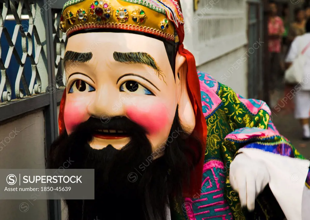 Thailand, Bangkok, Man in Chinese costume with papier-mache head and beard carried in parade celebrating local temple.