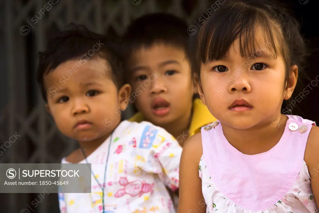 Thailand, Bangkok, Young children in late afternoon sun in front of shophouse entrance.