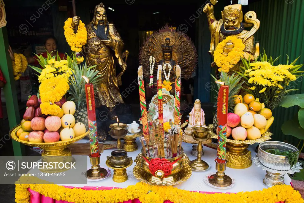 Thailand, Bangkok, Offerings on table with Guanyin Goddess of Mercy statue in centre celebrating local temple.