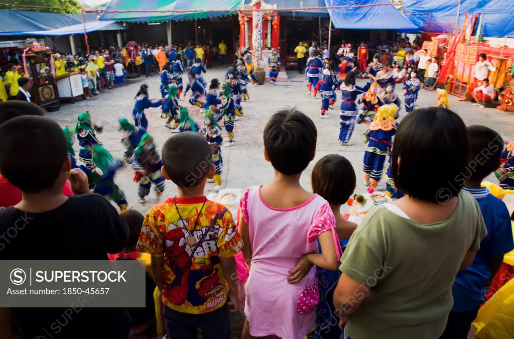 Thailand, Bangkok, Thai children watch dance troupe at local temple from elevated stage.