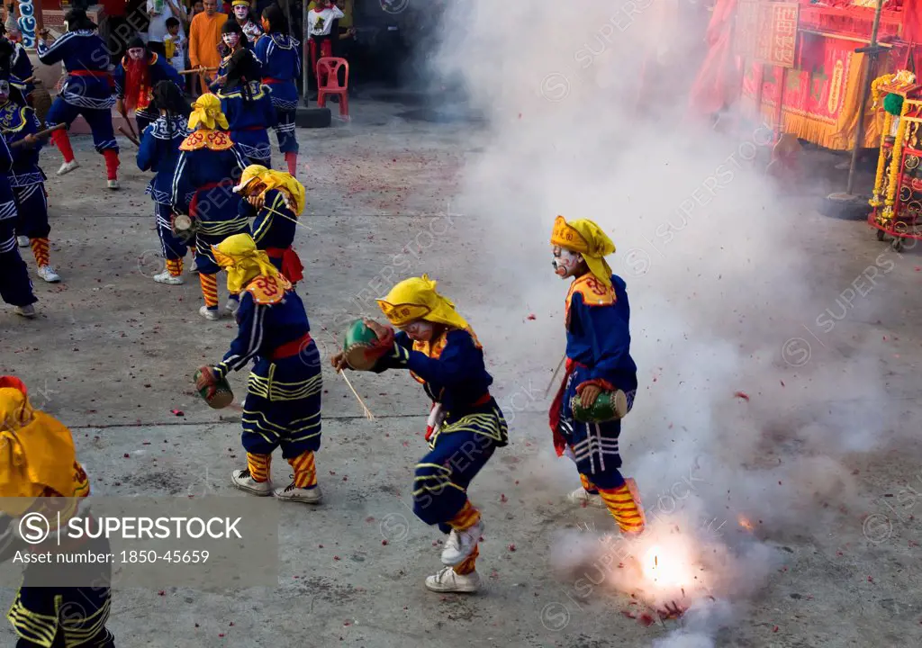 Thailand, Bangkok, Thai boys in Chinese character costume dancing and drumming with firecrackers exploding at local temple.