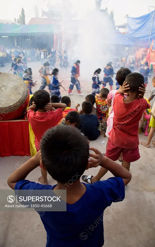 Thailand, Bangkok, Thai boys cover their ears watching performance with firecrackers exploding at local temple.
