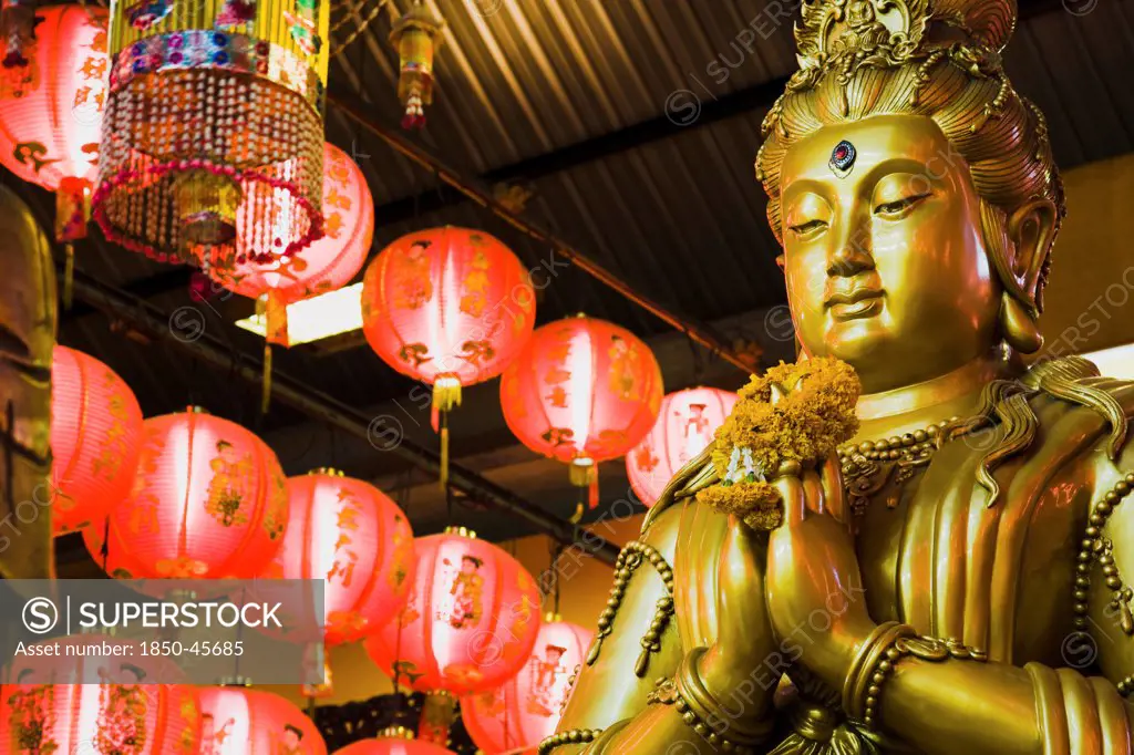 Thailand, Bangkok, Gold Guanyin Goddess of Mercy statue with red lanterns for Chinese New Year.