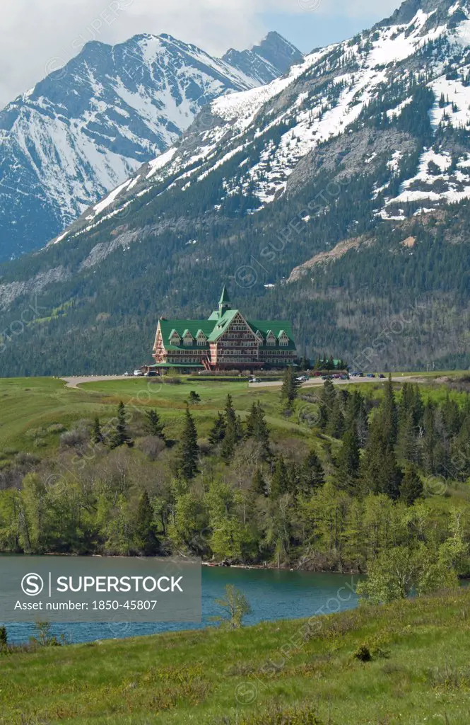 Canada, Alberta, Waterton Lakes NP, Prince of Wales Hotel at Waterton Lakes National Park a UNESCO World Heritage Site, Built of wood in 1927 by the American Great Northern Railway the hotel is a National Historic Site of Canada, Snow on Rocky Mountains, Green grass, Pine and Aspen trees and Linnet Lake.