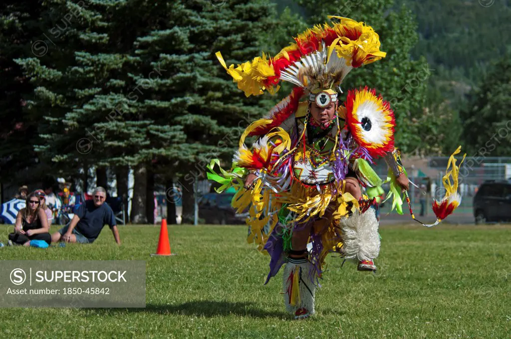 Canada, Alberta, Waterton Lakes National Park, Blackfoot dancer in the Men's Fancy Dance at the Blackfoot Arts & Heritage Festival Pow Wow organized by Parks Canada and the Blackfoot Canadian Cultural Society, Tourists sitting on grass watching spectacle, UNESCO World Heritage Site.