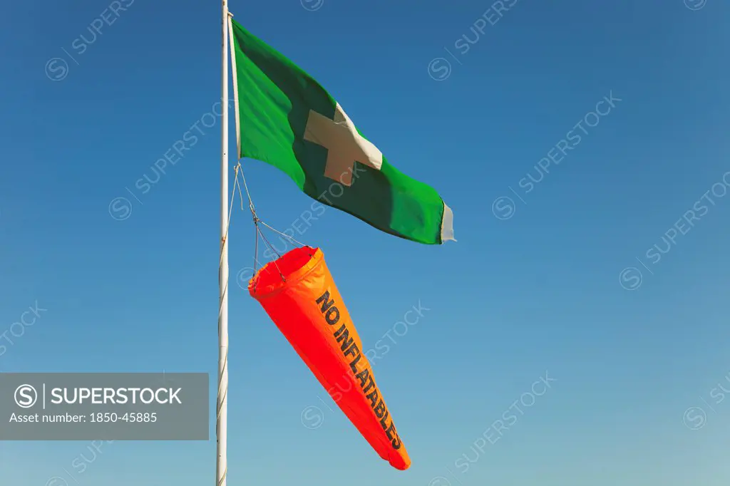 England, West Sussex, West Wittering Beach, Beach safety flags. White Cross on Green Flag signalling First Aid Point. Orange No Inflatables windsock.