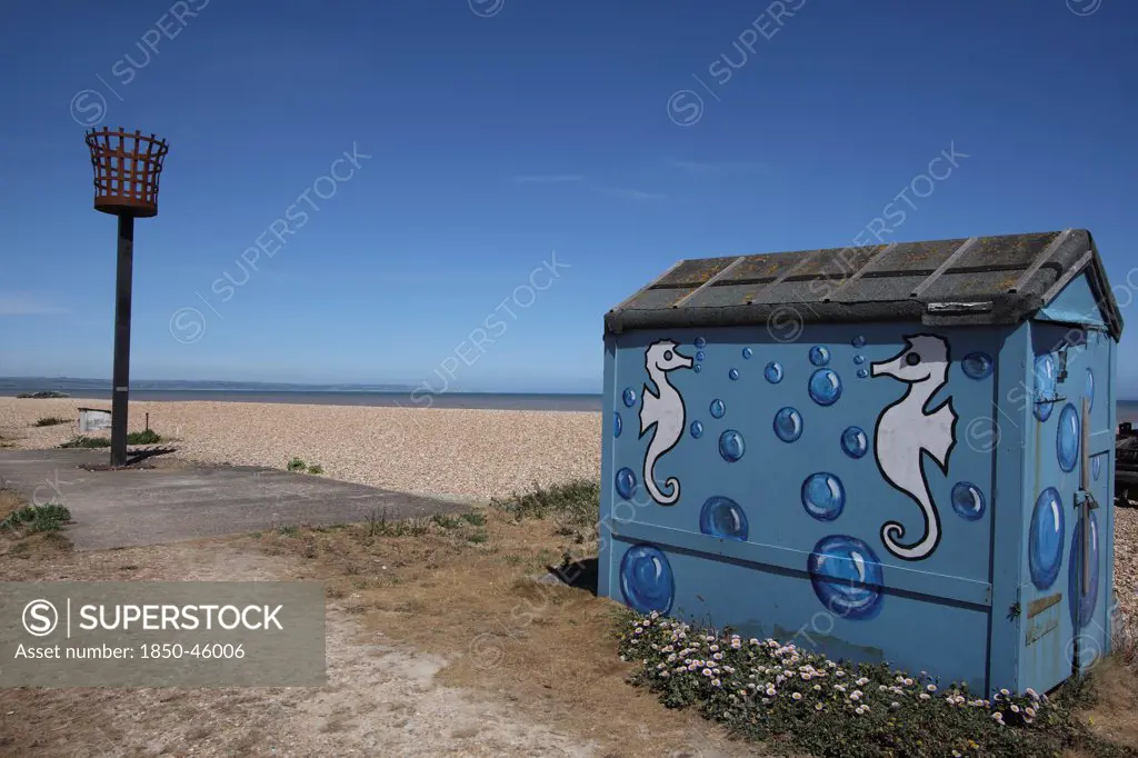 England, Kent, Romney Marsh, Littlestone Beach, Hut painted with Seahorse design and seafront torch beacon.
