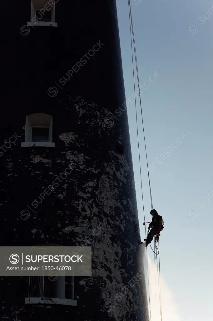 England, Kent, Romney Marsh, Dungeness, Man cleaning Lighthouse tower with pressure washer whilst abseiling.