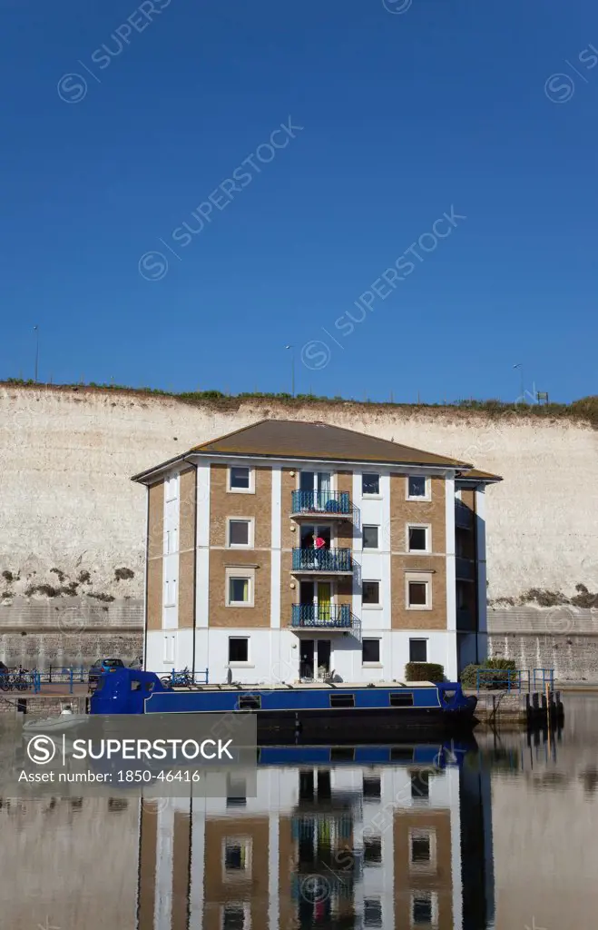 England, East Sussex, Brighton, apartment building in marina with moored barge and chalk cliffs behind.
