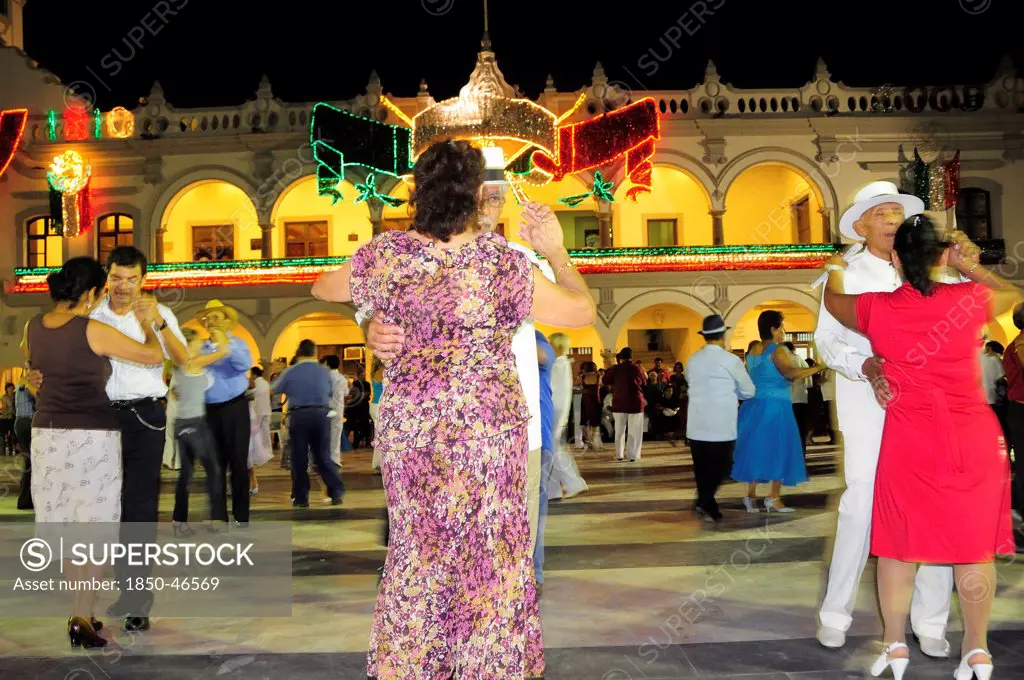 Mexico, Veracruz, Couples dancing in the Zocalo at night illuminated decorations in the national colours for Independence Day celebrations on building facade behind.