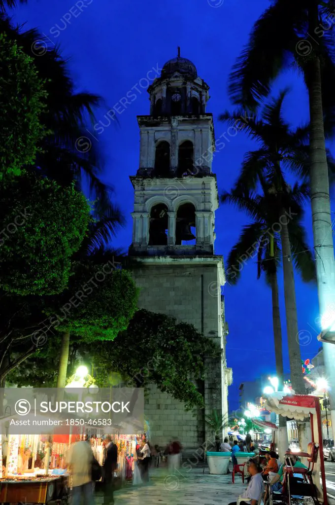 Mexico, Veracruz, Stalls in the Zocalo with the cathedral bell tower behind at night with illuminated street lights.