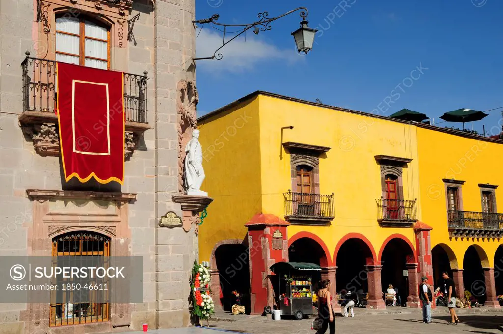 Mexico, Bajio, San Miguel de Allende, El Jardin Part view of Museo Casa de Allende and yellow painted arcades people and fruit juice vendor.