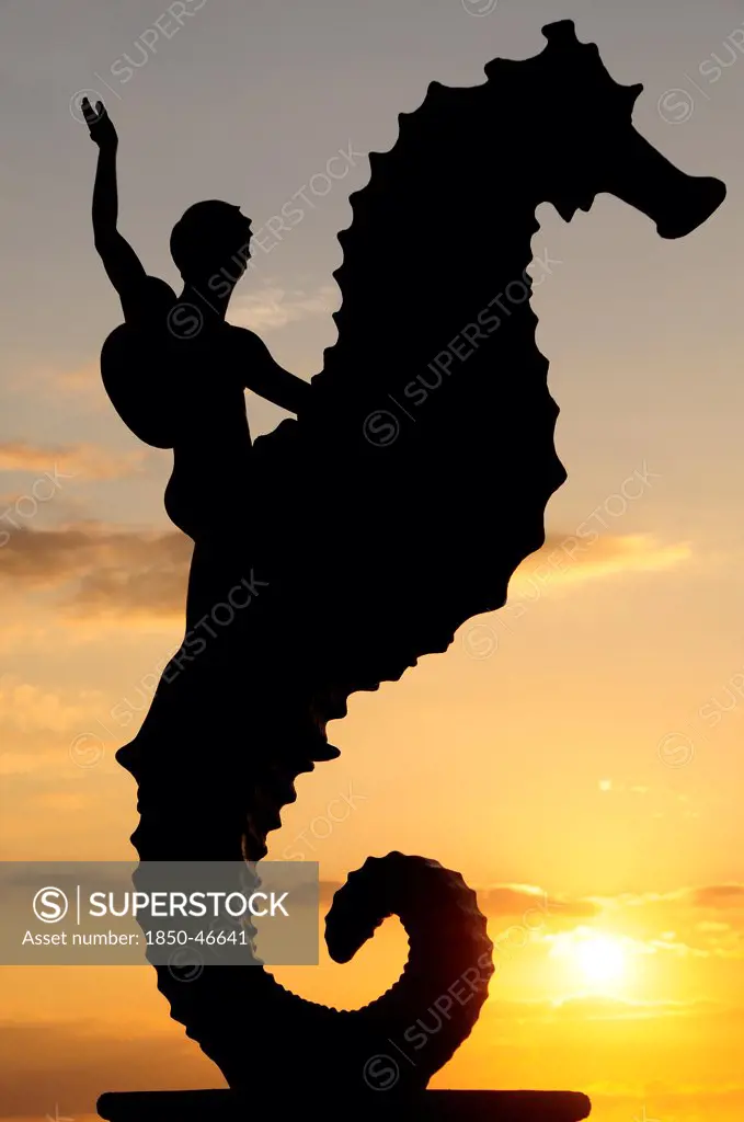 Mexico, Jalisco, Puerto Vallarta, Caballeo del Mar sculpture of boy riding a seahorse by Rafel Zamarripa silhouetted on the Malecon at sunset.