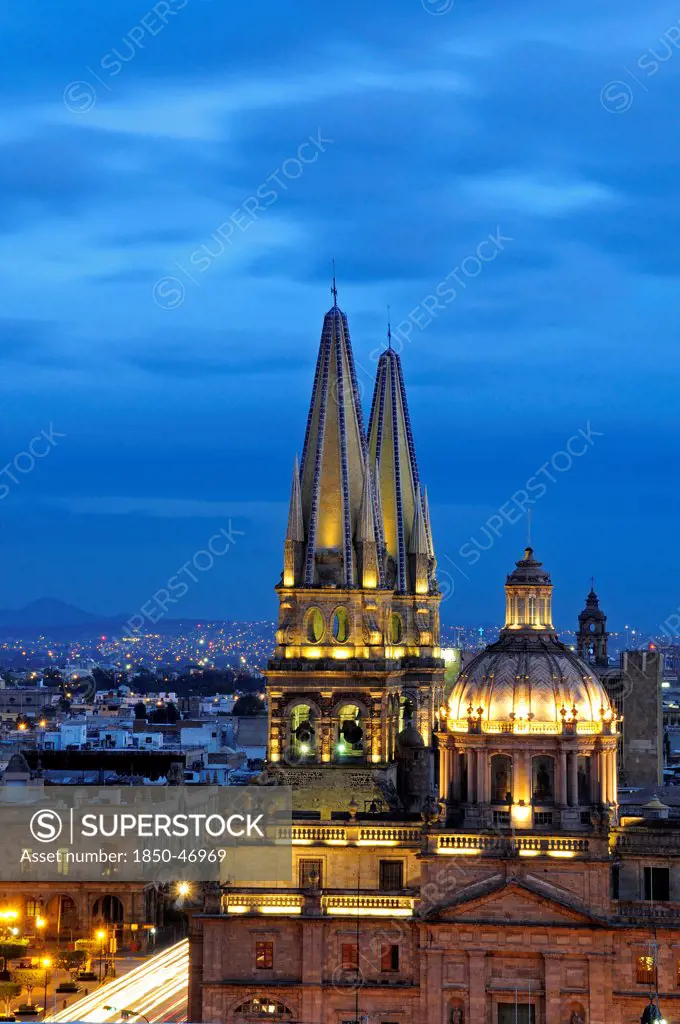 Mexico, Jalisco, Guadalajara, Cathedral domed roof and bell towers at night with city spread out behind.