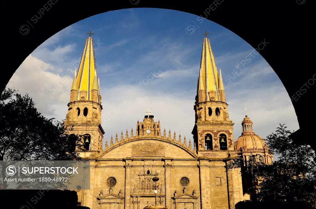 Mexico, Jalisco, Guadalajara, Plaza Guadalajara Exterior facade of cathedral and bell towers framed by archway in shadow.