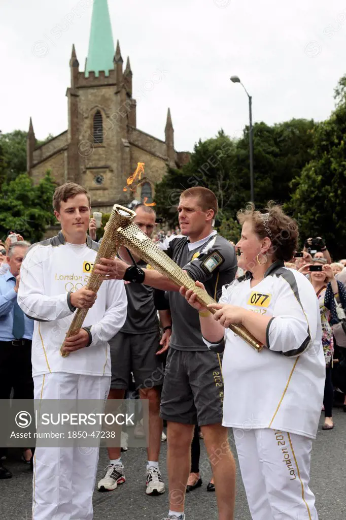 England, Kent, Tunbridge Wells, Olympic Torch relay runners handing over torch by exchanging the flame.