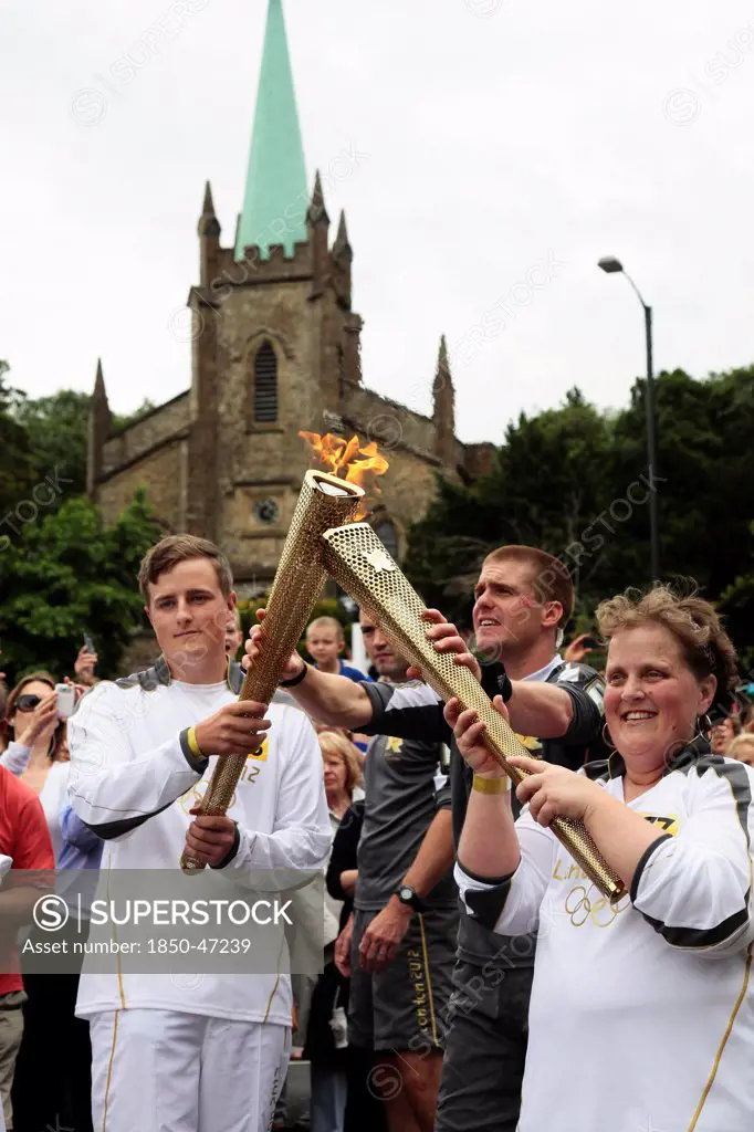 England, Kent, Tunbridge Wells, Olympic Torch relay runners handing over torch by exchanging the flame.