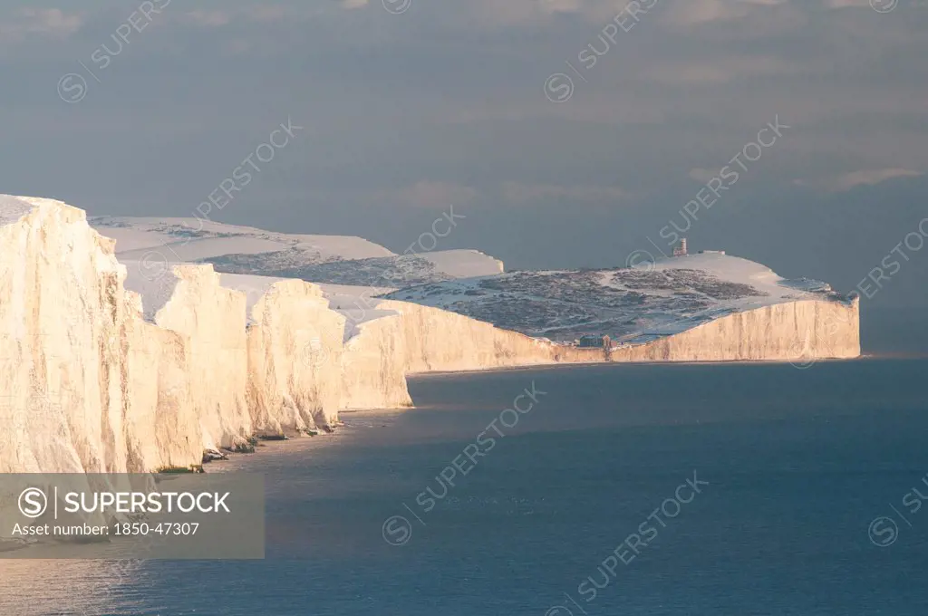 England, East Sussex, Seven Sisters, Snow covered coastline from Birling gap showing the coastguard Cottages in the foreground and Belle Tout lighthouse in the distance.