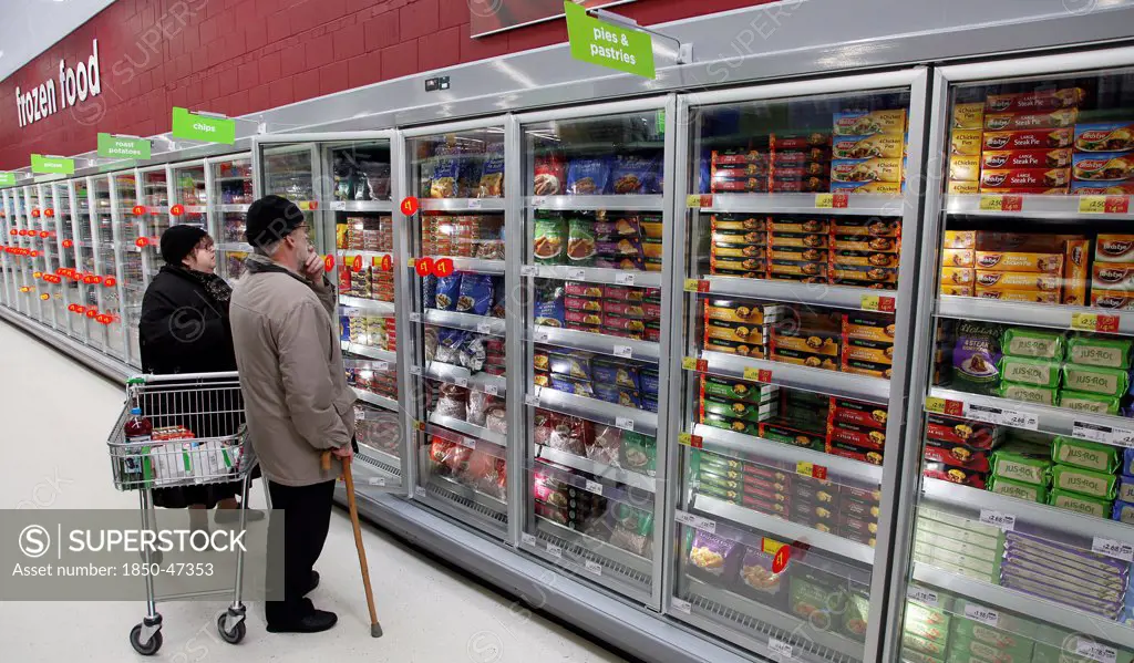 Shopping, Supermarket, Food, Elderly couple with shopping trolley looking at frozen goods in glass fronted freezer displays.