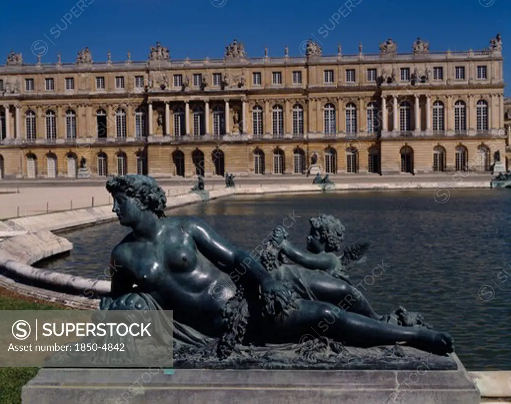 France, Ile De France, Yvelines, Versailles. Part View Of Palace With Bronze Reclined Statue Of Woman With Child Next To Pond