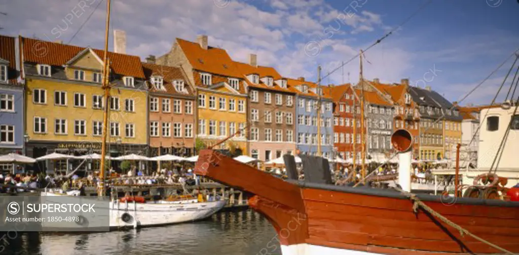 Denmark,  , Copenhagen, Boats On Nyhavn Canal With Pavement Cafes And Waterside Buildings Behind.