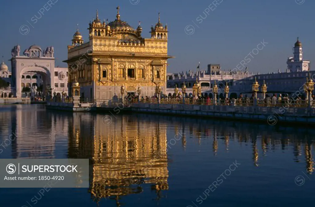India, Punjab, Amritsar, Golden Temple With Pilgrims And Visitors On Causeway Or The GuruS Bridge Leading To Temple Reflected In Rippled Surface Of Pool.
