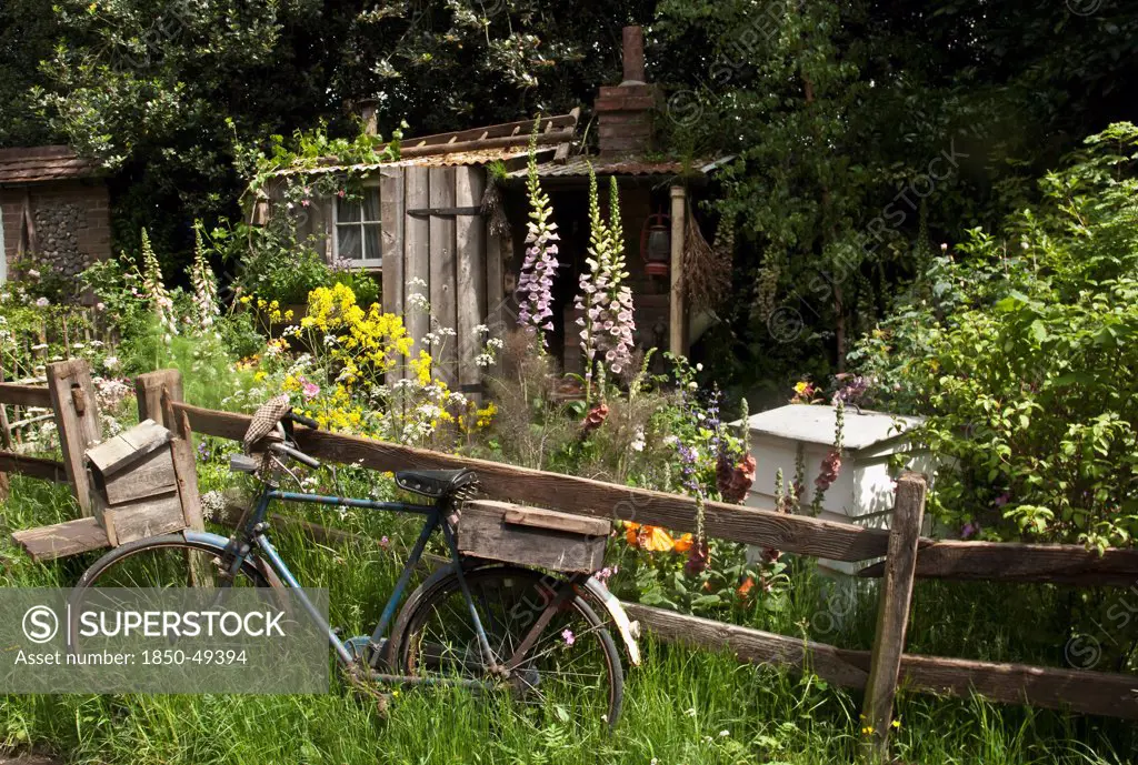 Chelsea Flowershow 2009, The Fenland Alchemist's Garden, Gold medal winner Best Courtyard Garden, designed by Stephen Hall and Jane Besser. Informal planting scheme with old bicycle leaning against wooden fence in foreground with flat cap hanging from the handlebars. Beehive, produce box and lean-to shed behind.