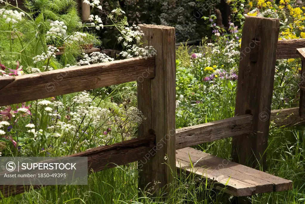 Wooden stile set into fence leading to area of soft, informal planting including cow parsley, fennel and wild grasses.
