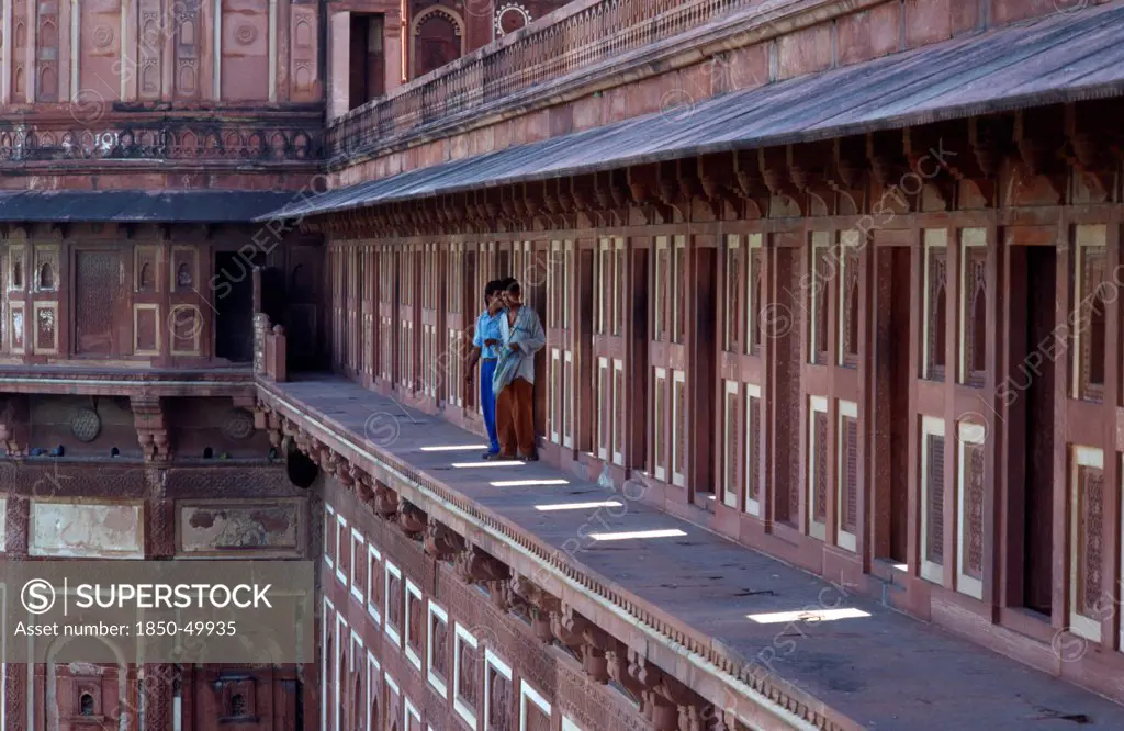 India, Uttar Pradesh, Agra, Taj Mahal. Two young men standing on open balcony of red and cream painted building.