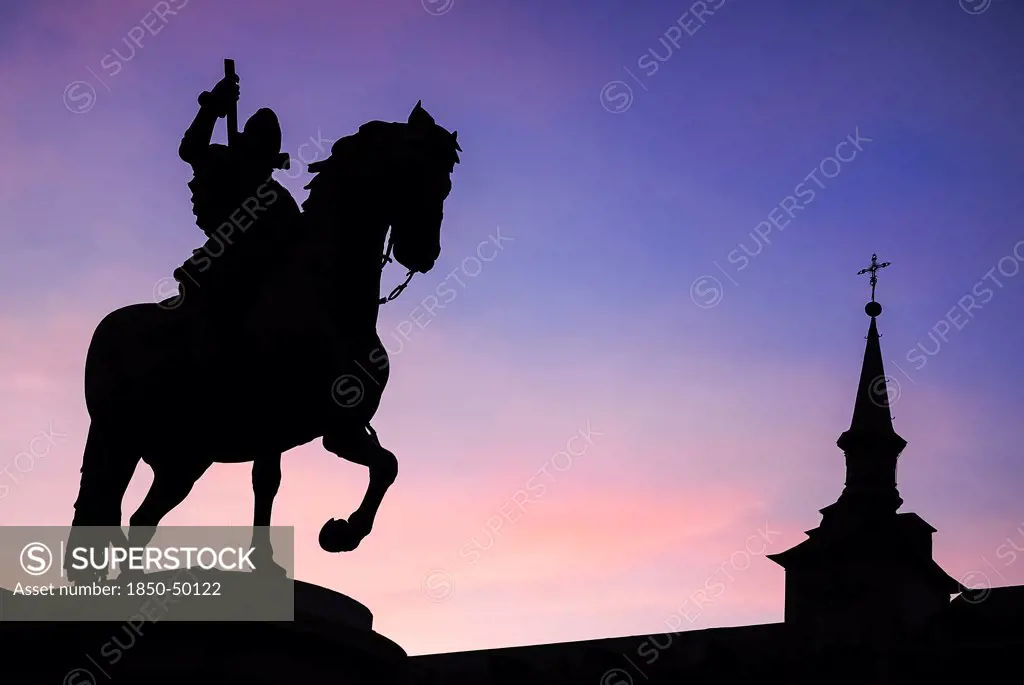 Spain, Madrid, Statue of King Philip II in Plaza Mayor silhouetted against evening sky.