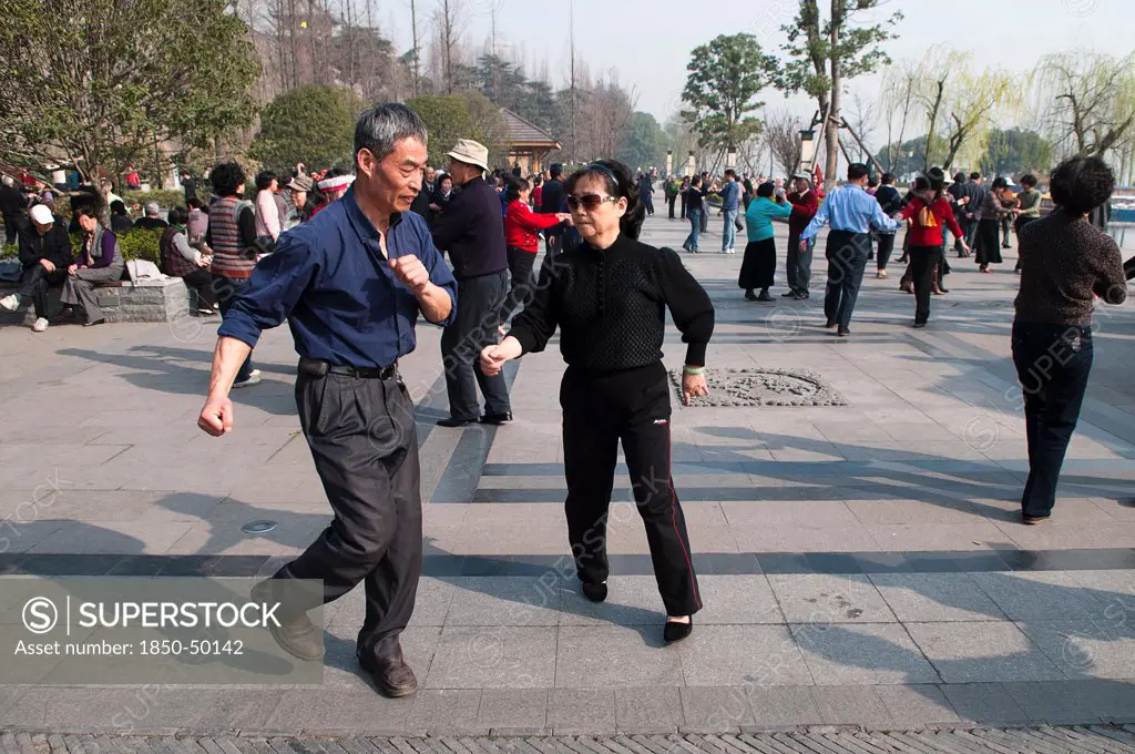China, Jiangsu, Nanjing, Retired couples dancing beneath the Ming city wall at Xuanwu Lake Park Couple in foreground swinging arms in modern dance.