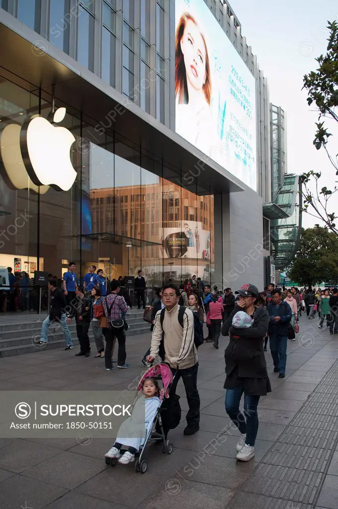 China, Shanghai, Modern young Chinese family with daughter in stroller and infant in sling stroll past the Apple store on Nanjing Lu Store staff and Security on steps at entrance evening light