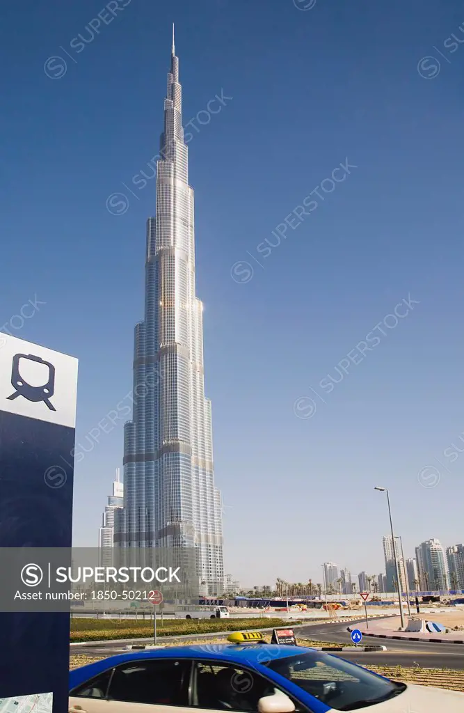 UAE, Dubai, Metro sign and taxi in front of Burj Khalifa tower.
