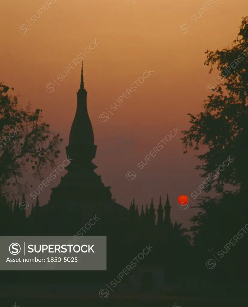 Laos, Vientiane, Pha That Luang Sacred Stupa Silhouetted Against Red Setting Sun And Orange Sky.