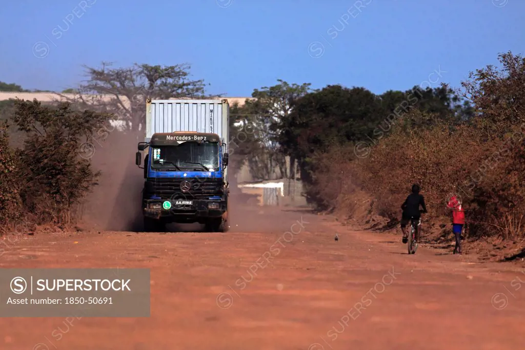 Gambia, Transport, Gambia heavy goods vehicle carrying sea container on unsurfaced red dirt road to terminal on the Bund Road.