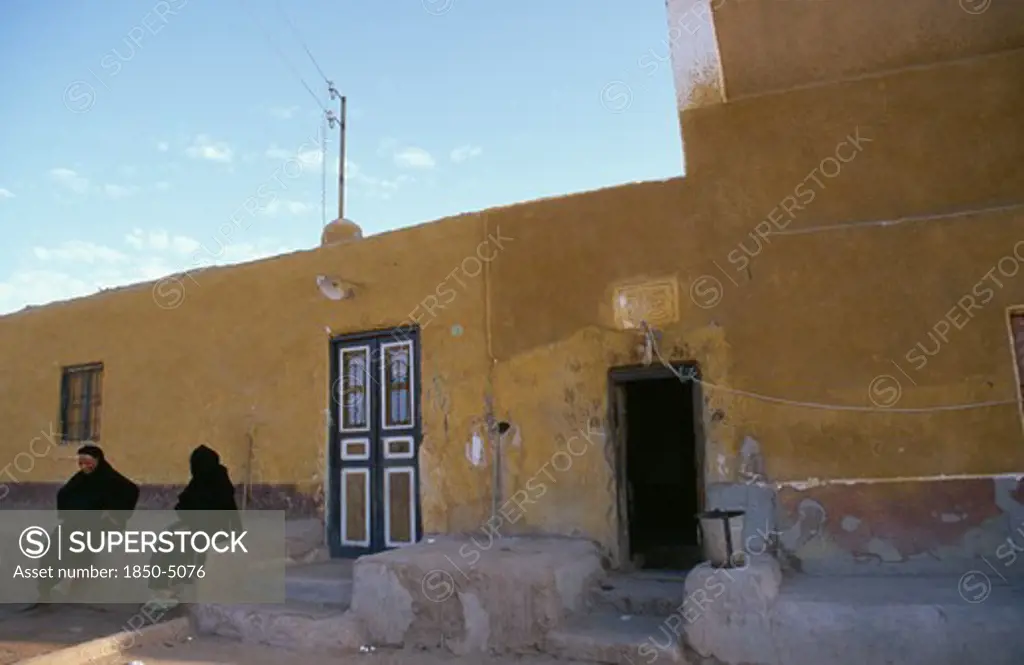 Egypt, Upper Egypt, Aswan, Two Muslim Women Seated Outside Yellow Coloured Building.