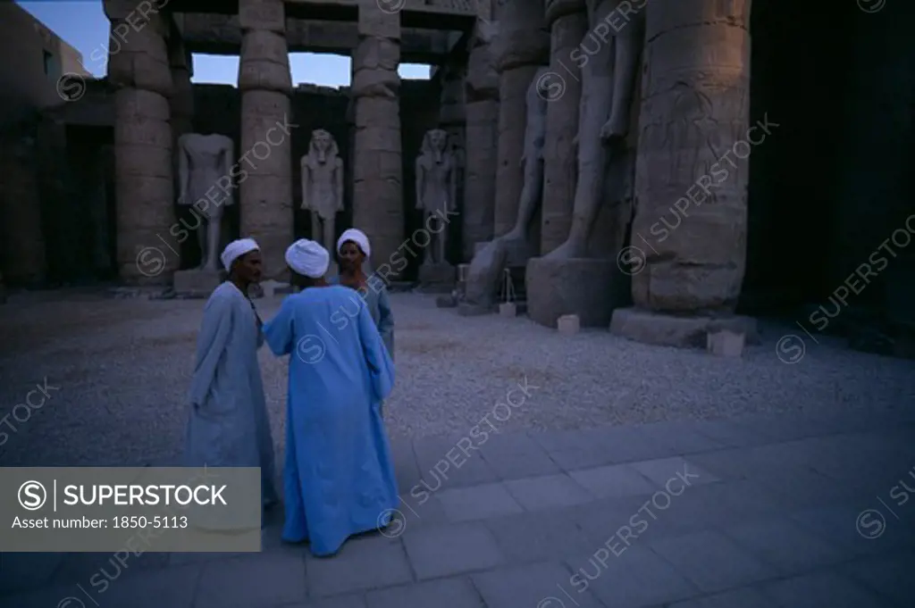 Egypt, Upper Egypt, Luxor, Group Of Three Men Talking Inside The Temple Of Luxor Statues In Background