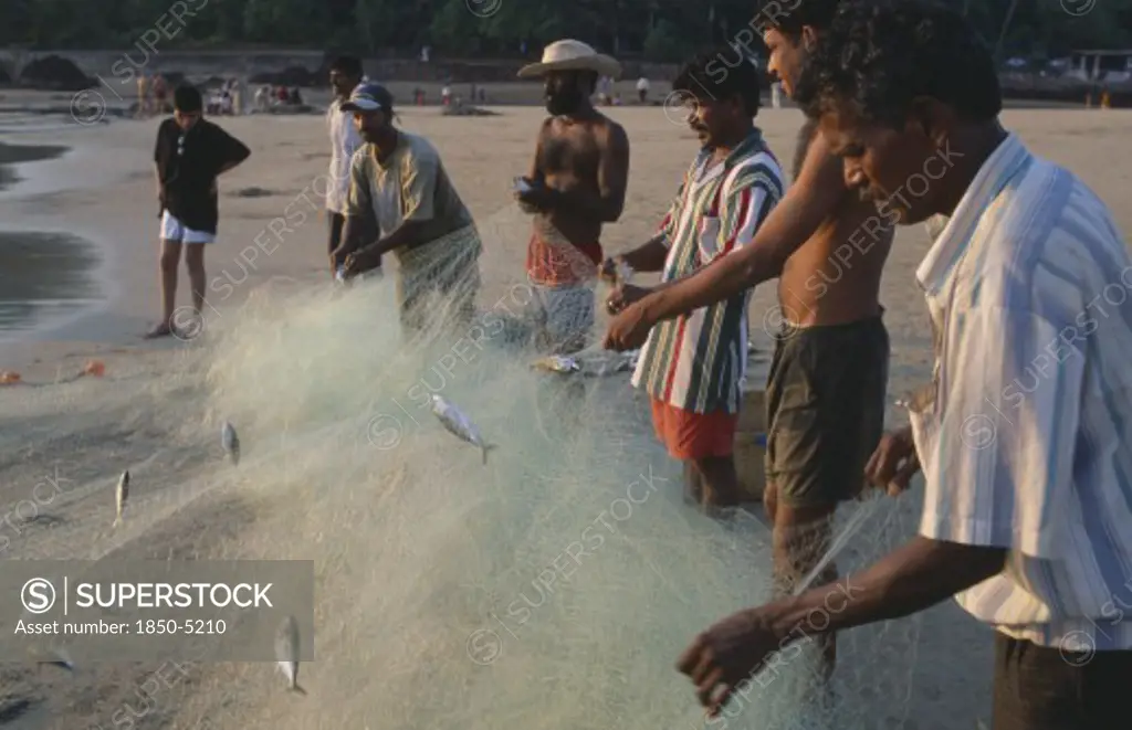 India, Goa, Calangute, Men Working On The Beach Sorting Fishing Net