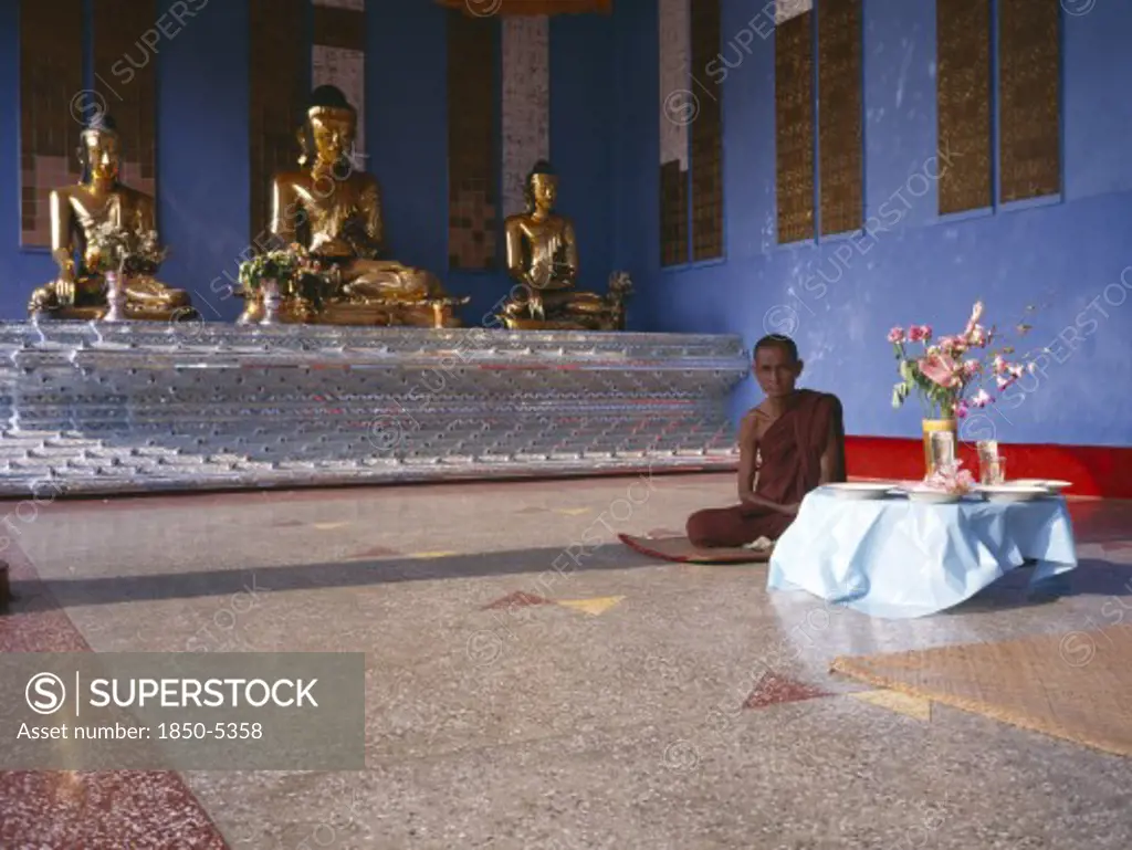Myanmar, Yangon, 'Shwedagon Pagoda Interior.  Monk Sitting Beside A Raised Altar With Three Seated, Golden Buddha Figures.   '