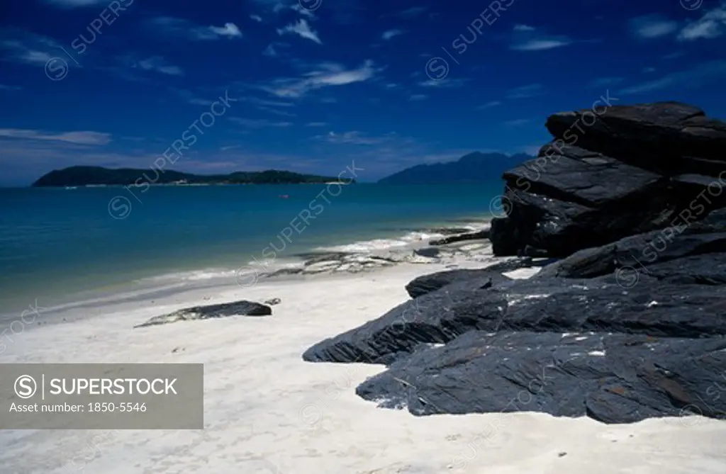 Malaysia, Kedah, Langkawi, Pantai Tengah Beach Looking Towards Pulau Rebak Besar Island With Rocks In The Foreground