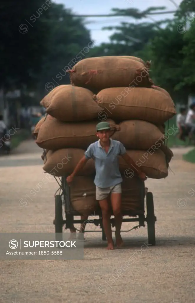 Vietnam, Transport, Man Pulling A Loaded Cart Stacked High With Sacks Behind Him.