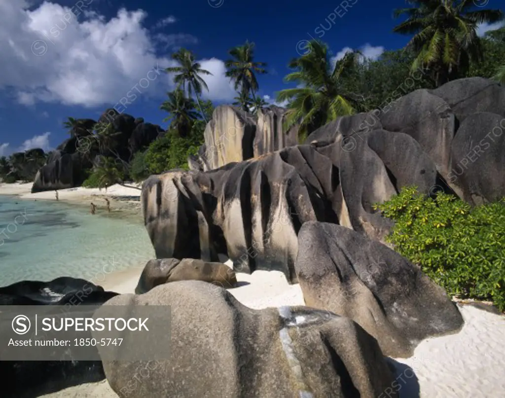 Seychelles, La Digue, Source De LArgent, 'Large, Smoothly Eroded Rocks With Graduated Colour Tones And Tidemarks.  Clear Blue Water, Palm Trees And Stretch Of White Sand Behind. '