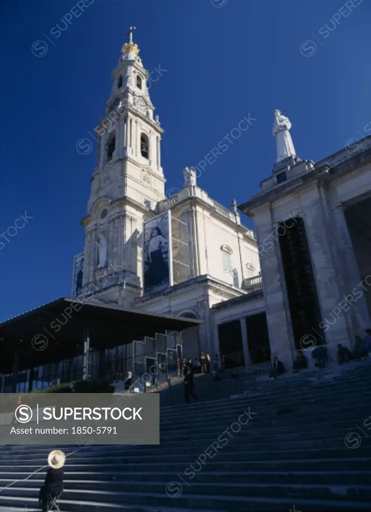 Portugal, Beira Litoral, Fatima, Woman Wearing Hat Seated By Steps Beneath The Church