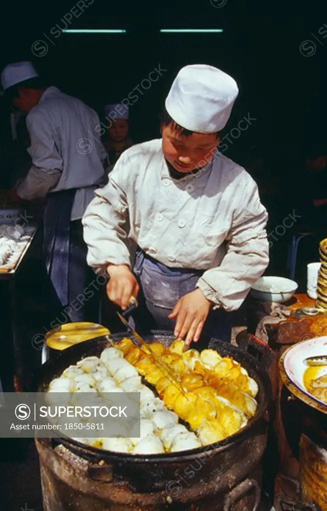 China, Shaanxi Province, Xian, Cook Turning Food Frying In Large Pan In Front Of Him.